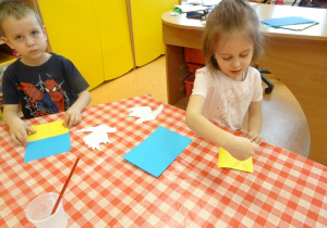 Dzieci naklejają żółty papier na kartkę.